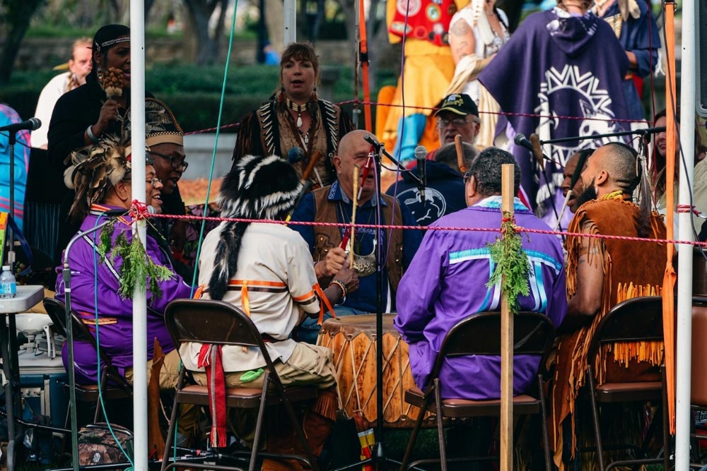 Singers in regalia gather around a large drum at a Pocasset Pokanoket Land Trust powwow.